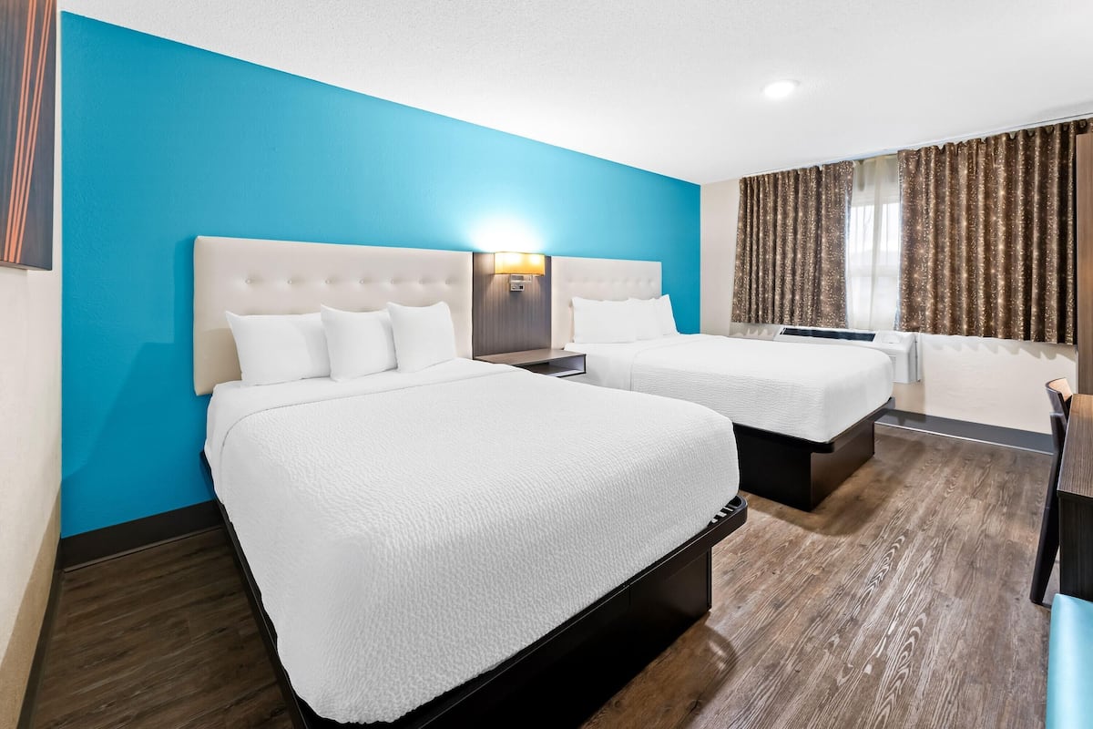 Habitación de hotel con dos camas, una pared de acento azul y un ventanal con cortinas.