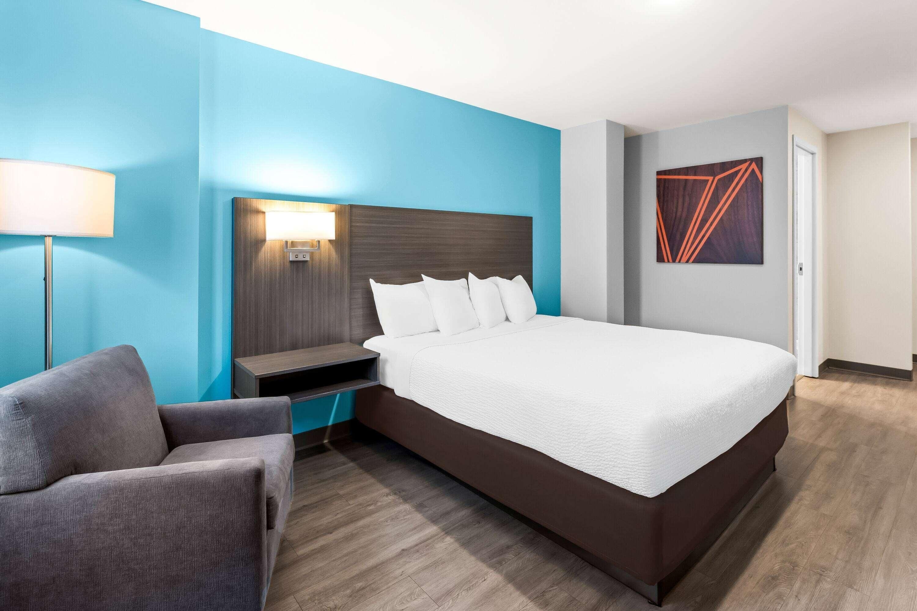A hotel room with a large bed, a bedside table, a chair, a lamp, and a painting on the wall.