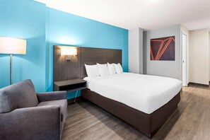Hotelkamer met een groot bed, nachtkastje, stoel, lamp en een schilderij aan de muur.