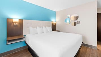 Una habitación de hotel moderna con una cama grande, una mesita de noche, una lámpara de pared y un espejo decorativo.