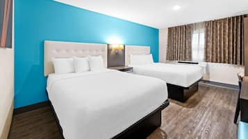 A hotel room with two beds, a blue accent wall, and a large window with curtains.