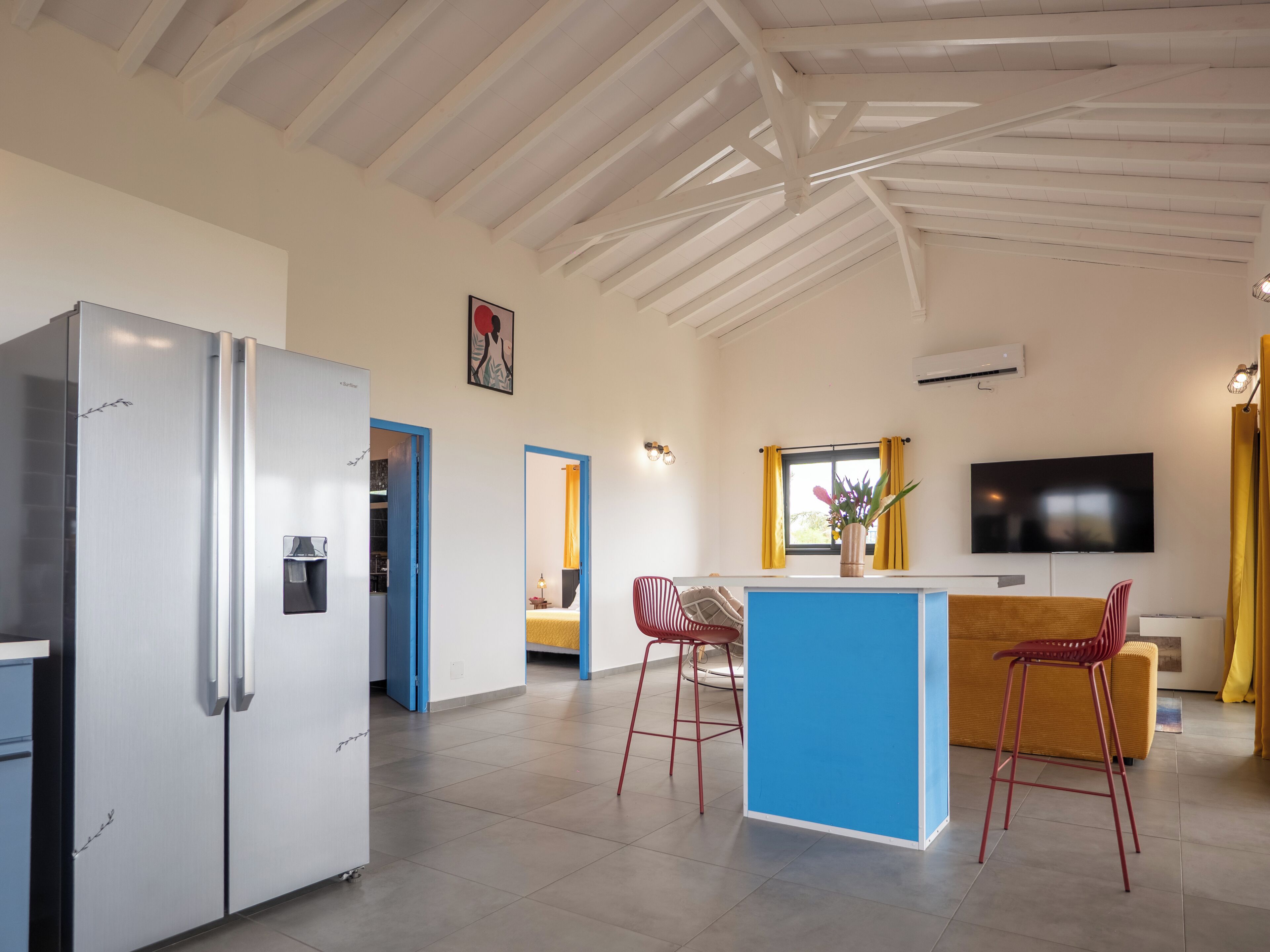 Eine moderne Küche mit einem weißen Kühlschrank, einer blauen Kücheninsel, roten Barhocker und einem an der Wand befestigten Fernseher.