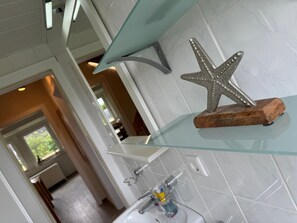 Bathroom features a clean, minimalist design with a white sink and glass shelf.