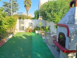 Un patio con césped artificial verde, plantas en macetas y una estructura de horno de piedra.
