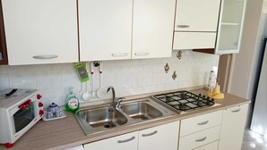 Een keuken met witte kastjes, een roestvrijstalen spoelbak, een gasfornuis, een magnetron en een afwassysteem.