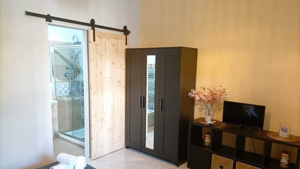 Een moderne slaapkamer met een schuifglazen deur naar een balkon, een donkere kledingkast, een flatscreen televisie en netjes opgevouwen handdoeken op de vloer.