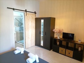 Un dormitorio moderno con puerta de cristal corredera que da a un balcón, un armario oscuro, un televisor de pantalla plana y toallas dobladas ordenadamente en el suelo.