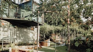 Un'area esterna moderna con un vialetto in cemento, ringhiere in metallo e una vegetazione rigogliosa tra cui alberi e arbusti.