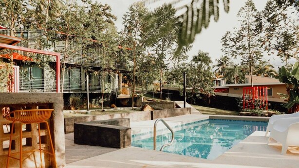 A swimming pool with a concrete deck, surrounded by trees and a red structure.