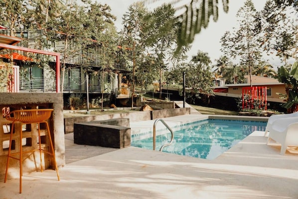 A swimming pool with a concrete deck, surrounded by trees and a red structure.