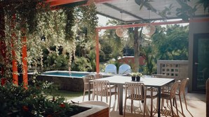 An outdoor patio with a pool, surrounded by wooden furniture and hanging plants.