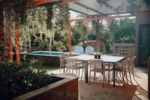 An outdoor patio with a pool, surrounded by wooden furniture and hanging plants.
