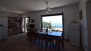 A dining area with a table and chairs, a ceiling fan, and a view of the sea through a large window. - Villa Roccella Ionica with Sea View (Roccella Jonica)