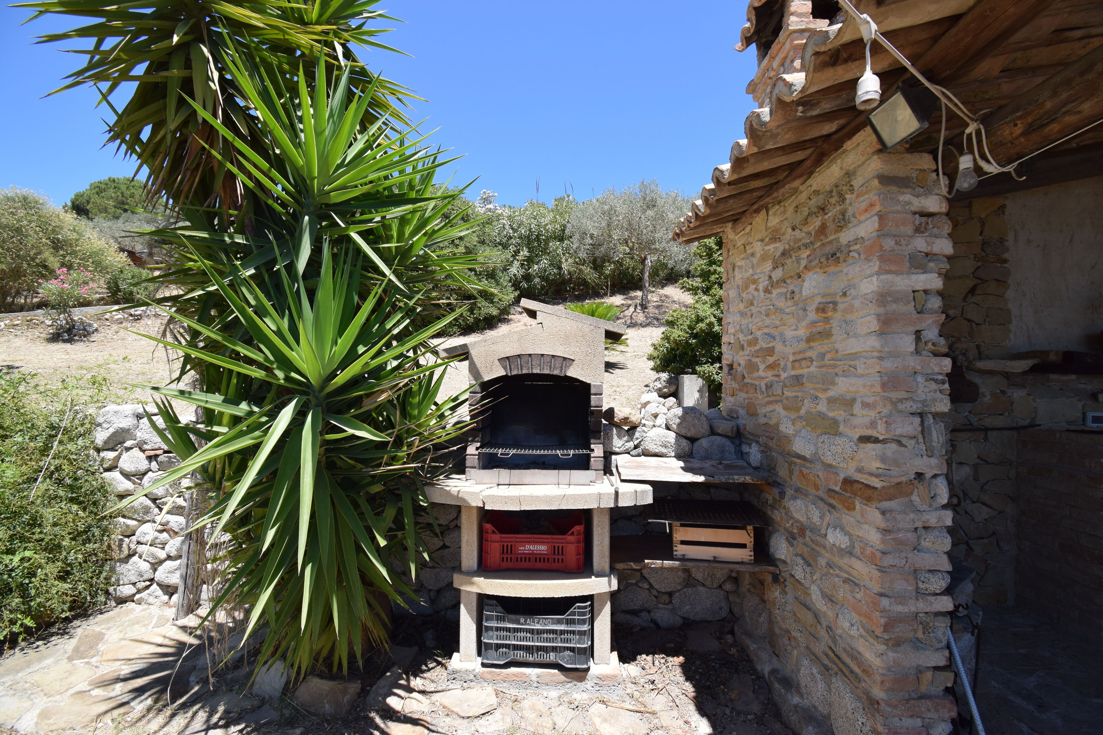 A stone building with a brick fireplace, surrounded by greenery and a clear blue sky.