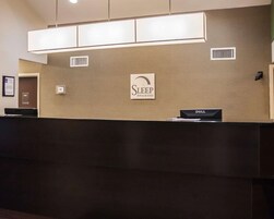 Una mesa de recepción con un cartel de Sleep Inn & Suites, un computador Dell y una rejilla de ventilación en la pared.