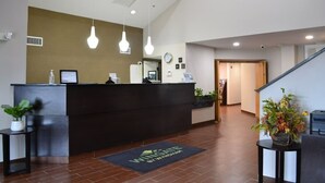 A reception area with a dark reception desk, hanging light fixtures, a clock, and a staircase leading to another floor. - Wingate by Wyndham Bel Air I-95 Exit 77A / APG Area (Edgewood)