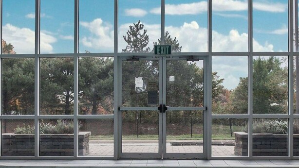 A pool area with a clear view of the pool through large windows, a sign indicating an exit, and a tiled pool edge. - Wingate by Wyndham Bel Air I-95 Exit 77A / APG Area (Edgewood)