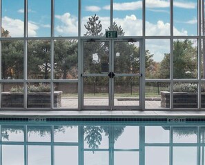A pool area with a clear view of the pool through large windows, a sign indicating an exit, and a tiled pool edge. - Wingate by Wyndham Bel Air I-95 Exit 77A / APG Area (Edgewood)