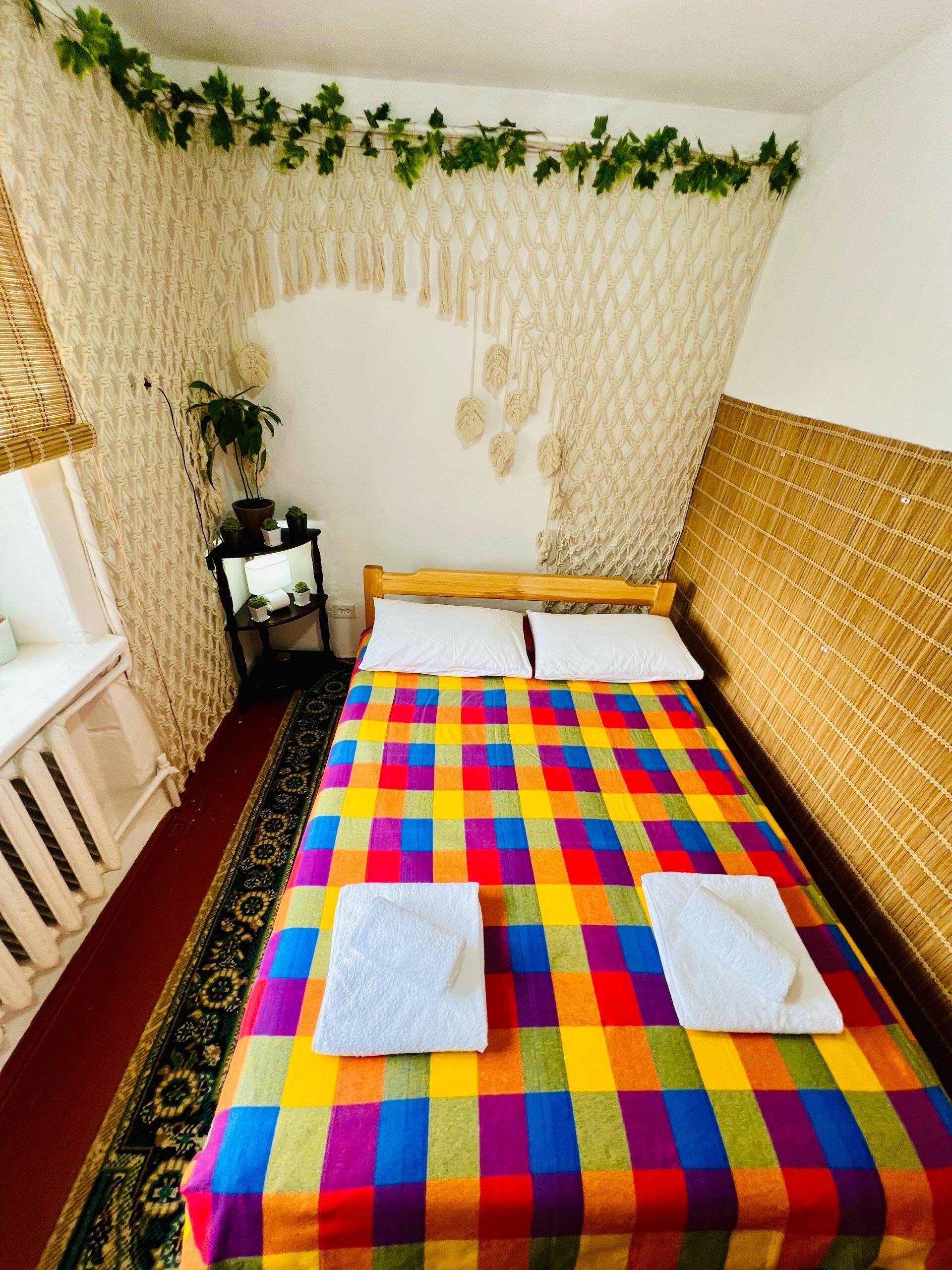 Una habitación con cama, mesita de noche, planta en maceta y decoración de macramé en la pared.