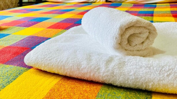 A bed with a colorful quilt, a rolled white towel, and a macrame wall hanging. - DADOW Apartments (Naryn)