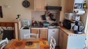 A compact kitchen with a dining table, chairs, a microwave, a coffee maker, and various kitchen utensils. - Villa Géraniums Apt n°4 (Mont-Dore)