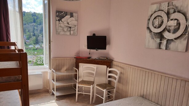 A room with a bed, two chairs, a desk with a computer, a TV, and artwork on the walls. - Villa Géraniums Apt n°4 (Mont-Dore)