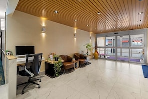 Un espace d’accueil doté d’un plafond en bois, d’un comptoir de réception, d’un téléviseur, de fauteuils en cuir, d’une plante en pot et d’un grand vase.