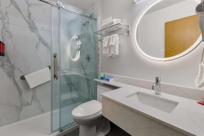 Un baño moderno con ducha de vidrio, inodoro blanco, tocador con lavamanos y espejo, y un perchero para toallas.