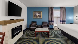 Habitación de hotel con televisor de pantalla plana, chimenea, dos sillones de cuero, cama y un cuadro en la pared.