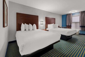 Une chambre d’hôtel avec deux lits, une tête de lit en bois, une table de chevet avec une lampe, une fenêtre avec des rideaux et une moquette à motifs.