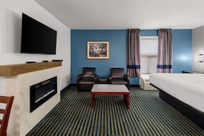 Une chambre d’hôtel équipée d’un téléviseur à écran plat, d’une cheminée, de deux fauteuils en cuir, d’un lit, d’une petite table et d’un tapis à motifs.
