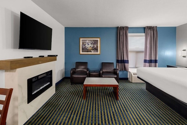 Ein Hotelzimmer mit Flachbildfernseher, Kamin, zwei Ledersesseln, einem Bett, einem kleinen Tisch und einem gemusterten Teppich.