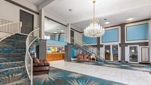 A spacious lobby with a grand staircase, a chandelier, and a reception desk.