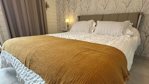 A bedroom with a large bed, a headboard, a nightstand with a lamp, and a wall with a tree pattern.
