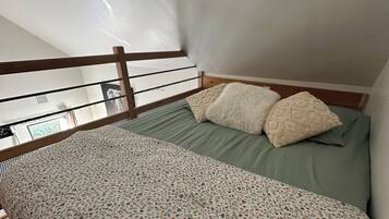 A bedroom with a bunk bed, a green bedspread, two fluffy pillows, and a wooden headboard.