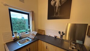 A compact kitchen with wooden cabinets, a stainless steel stove, and a window with a view of greenery.
