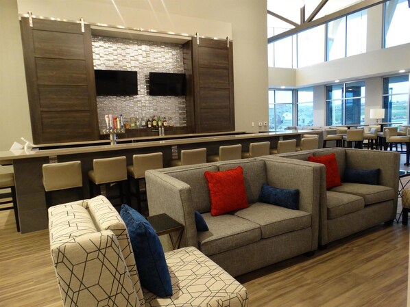 A modern lounge area with a bar, seating, and large windows. - Stone Hill Lawrence Trademark Collection by Wyndham (Lawrence)
