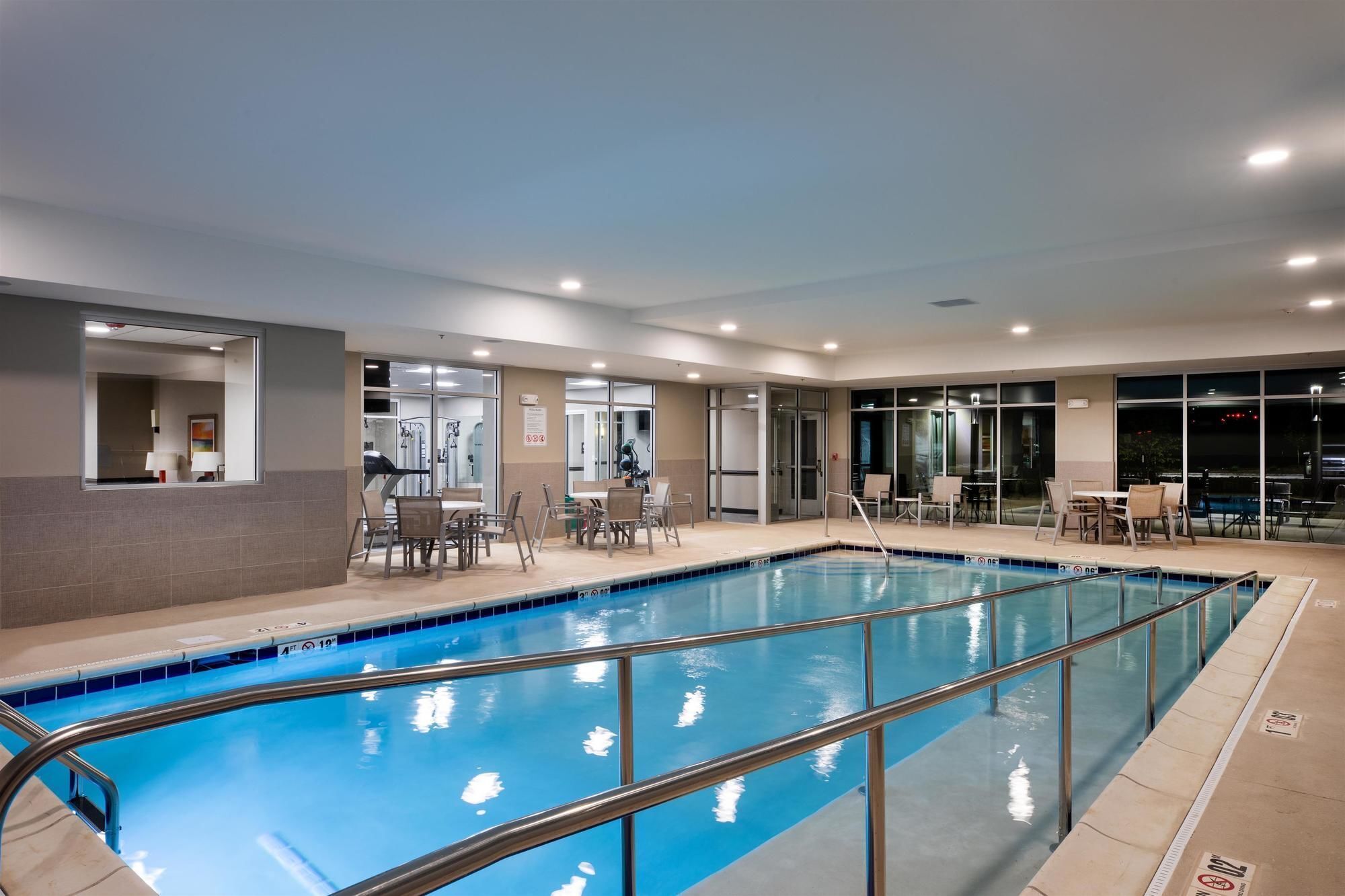 An indoor swimming pool with a clear view of the pool area, adjacent seating, and a glass-enclosed room with exercise equipment.