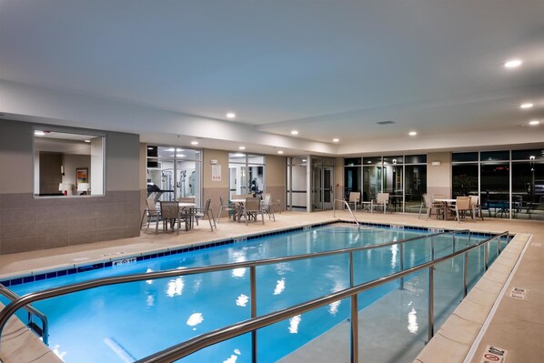 An indoor swimming pool with a clear view of the pool area, adjacent seating, and a glass-enclosed room with exercise equipment. - Stone Hill Lawrence Trademark Collection by Wyndham (Lawrence)