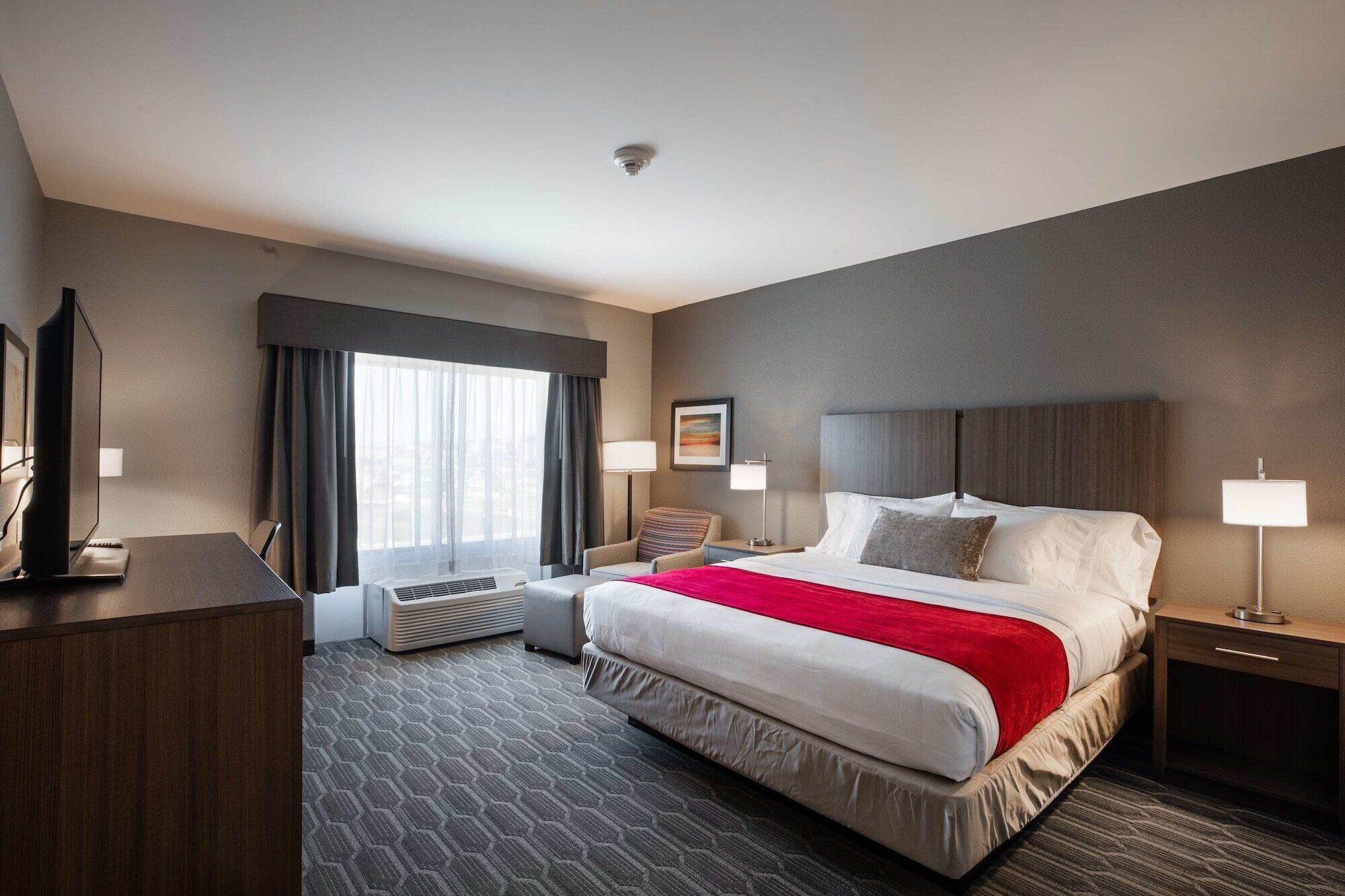 Een hotelkamer met een groot bed, een bureau met een computer, een stoel, een televisie en een raam met gordijnen.