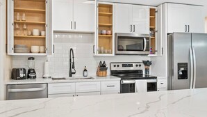Eine moderne Küche mit weißen Schränken, einer eingebauten Mikrowelle, einem Edelstahlkühlschrank, einem Gasherd und einer Kaffeemaschine.