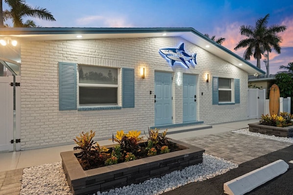 A white brick building with a shark sign, two doors, and a small garden area with plants.