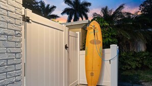 Ein weißes Holztor, an dem ein Surfbrett anlehnt.