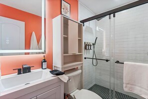 A modern bathroom with a white sink, a toilet, and a glass shower enclosure. - Shark Tank Cocoa Beach • 2 Units • Perfect for Families•Walk to Beach, Bars, & Shops (Cocoa Beach)