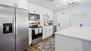 A modern kitchen with white cabinets, stainless steel appliances, a microwave, and a built-in oven. - The Shark Tank: Coastal Modern, Walk to Beach, Shops & Downtown Cocoa Beach (Cocoa Beach)