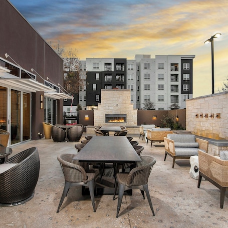 An outdoor patio area with a stone fireplace, wicker furniture, and a view of apartment buildings in the background.. Doubletree By Hilton San Antonio Northwest