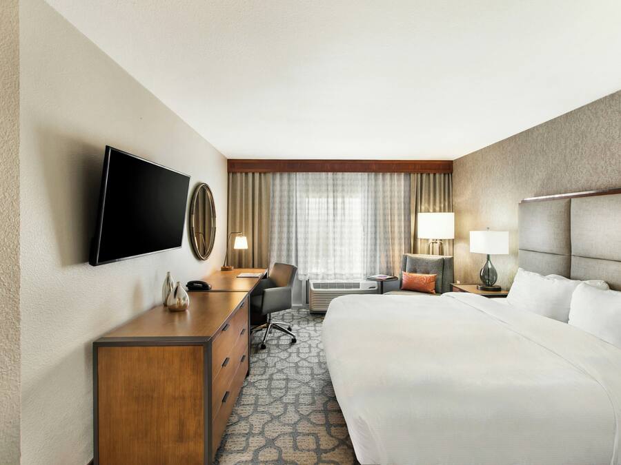 Een hotelkamer met een bed, bureau, stoel, televisie en een raam met gordijnen.