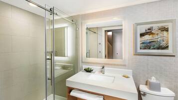 A modern bathroom with a glass shower enclosure, a white sink with a mirror, and a framed artwork on the wall.