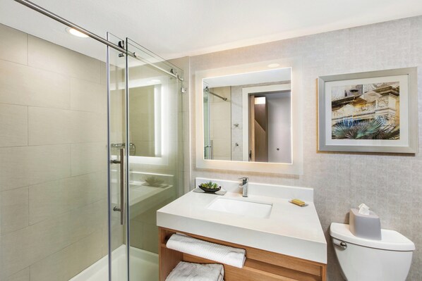 Un baño moderno con cabina de ducha de vidrio, un lavamanos blanco con espejo y una obra de arte enmarcada en la pared.