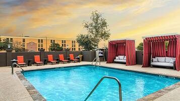 A swimming pool with lounge chairs and a covered seating area.